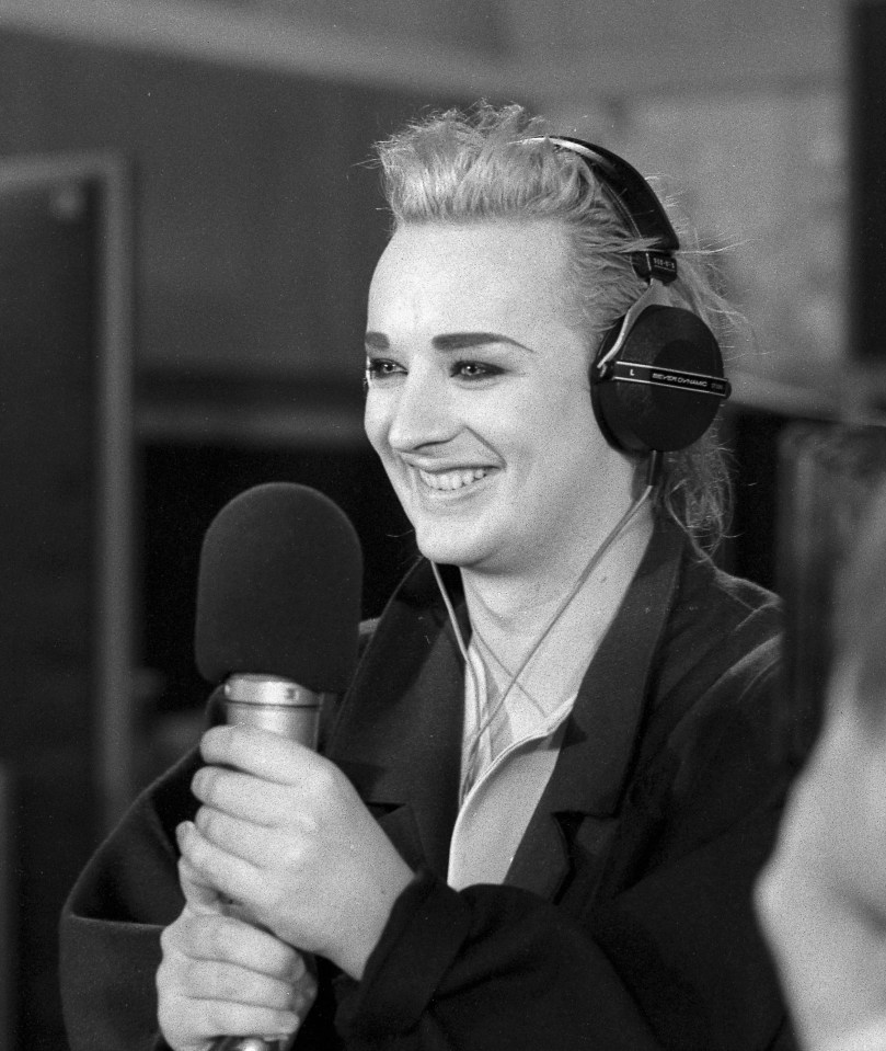 a woman wearing headphones holds a microphone and smiles