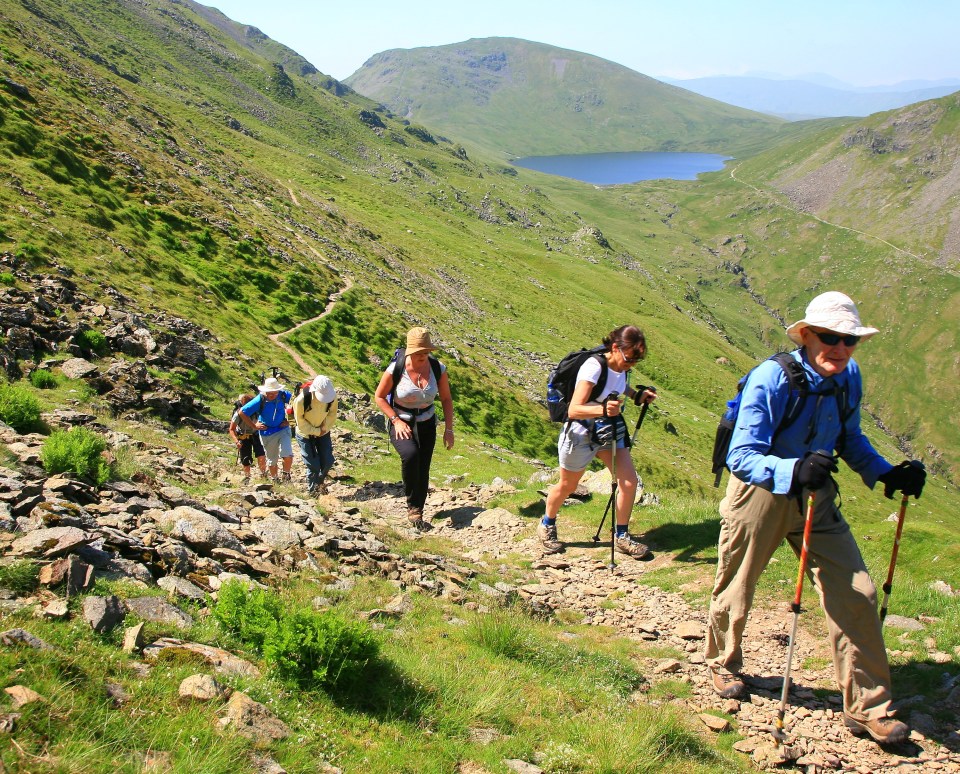 a group of people hiking up a hill with a lake in the background