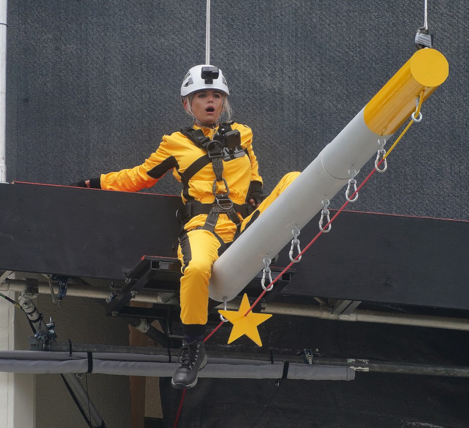 a woman in a yellow jumpsuit is sitting on a pole with a yellow star on it