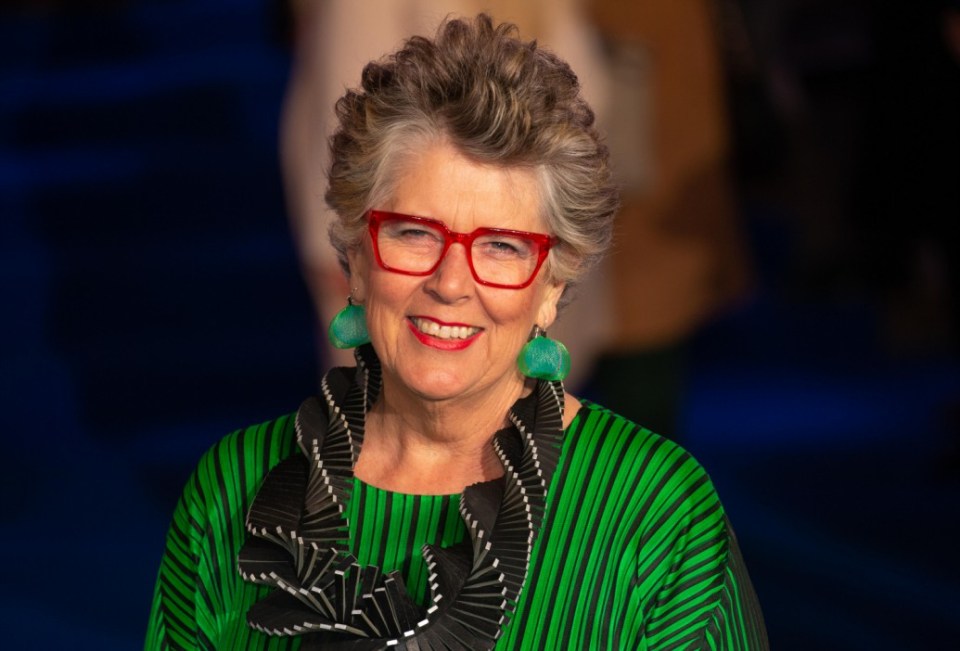 a woman wearing red glasses and green earrings smiles for the camera