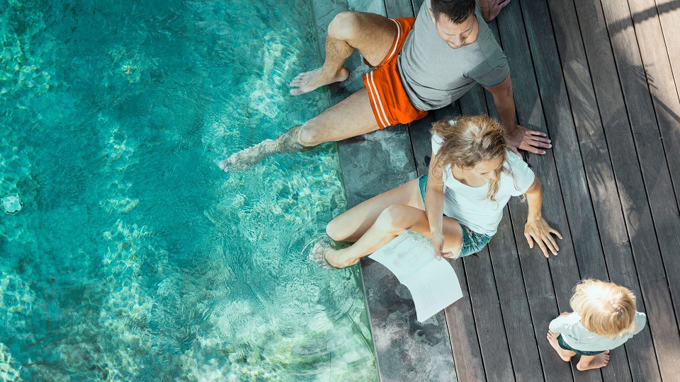 a family sits on the edge of a swimming pool