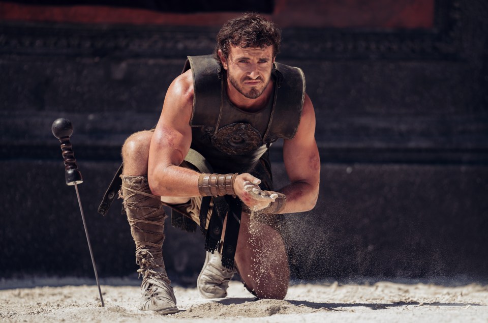 a man in a gladiator costume is kneeling in the sand