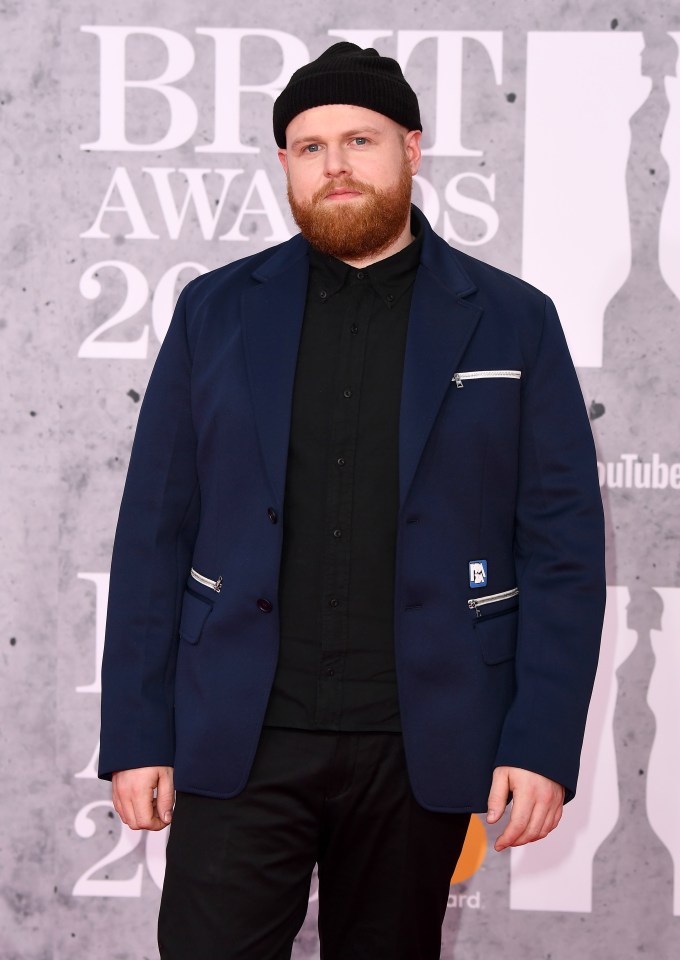 a man with a beard is standing on a red carpet at the brit awards