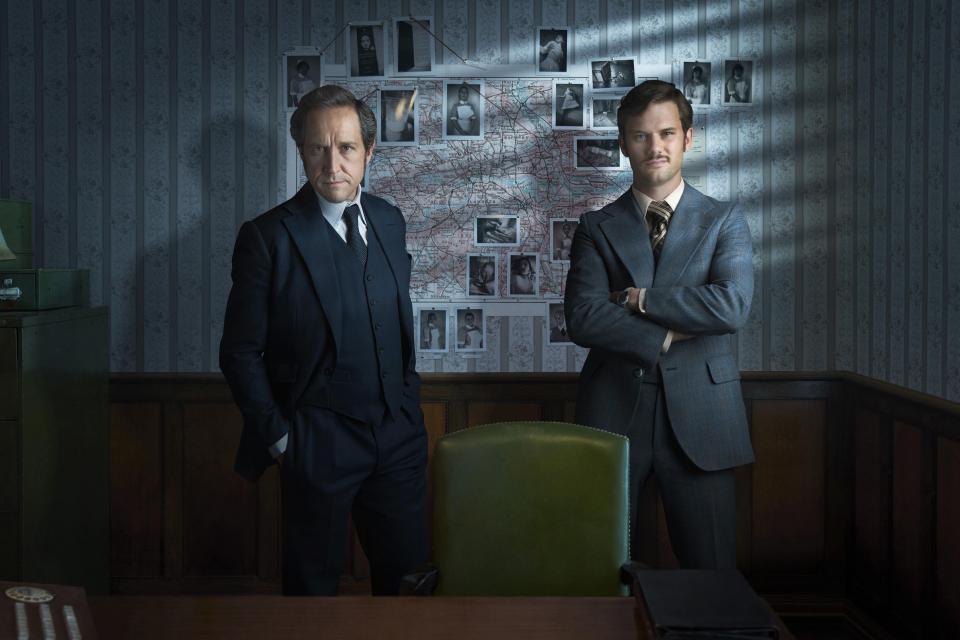 two men standing in front of a bulletin board with pictures on it