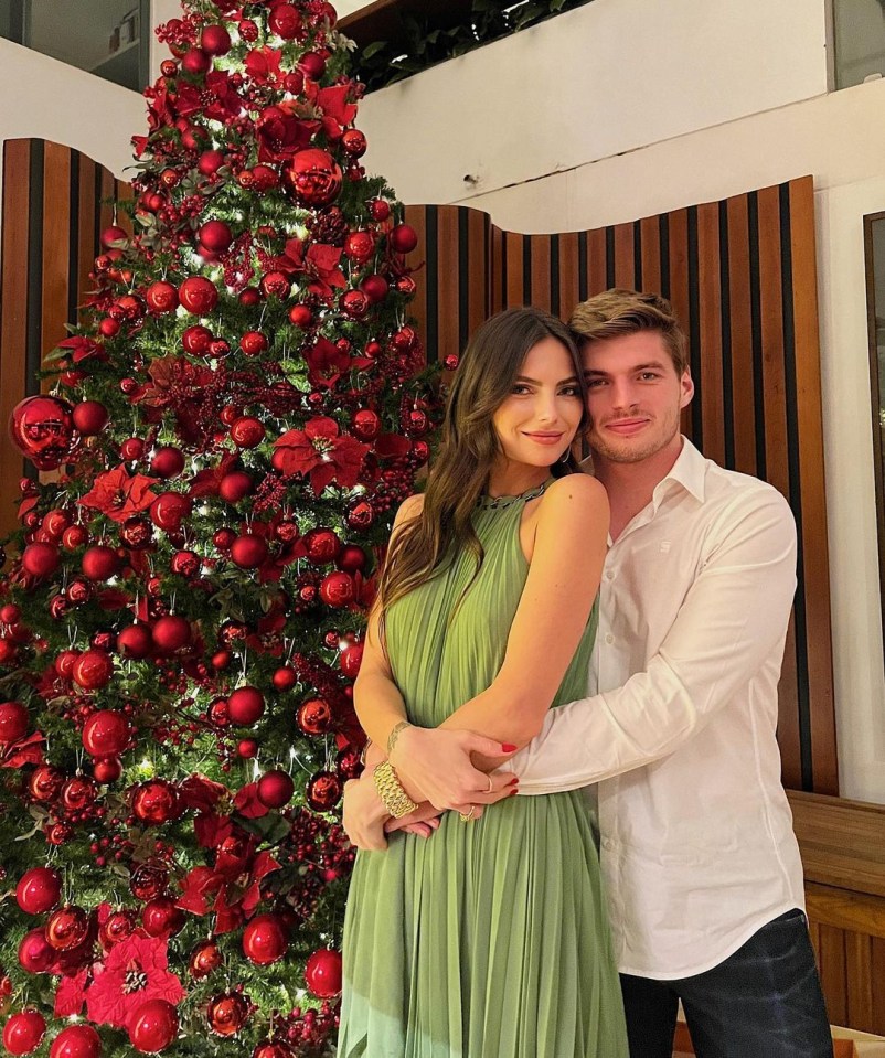 a man and woman pose in front of a christmas tree