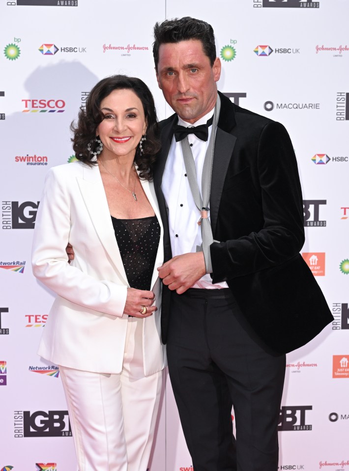 a man and woman are posing for a picture on a red carpet sponsored by tesco