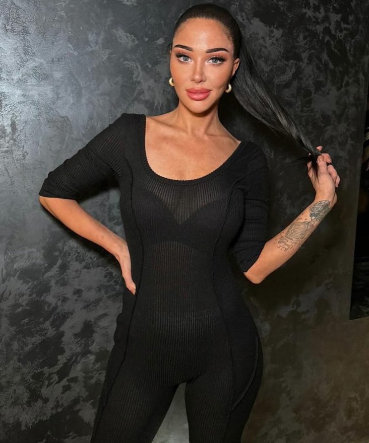 a woman with a tattoo on her arm is wearing a black jumpsuit