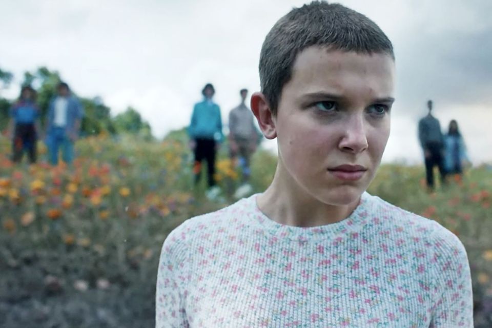 a girl with short hair is standing in a field of flowers