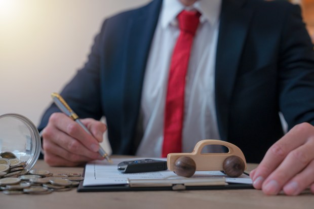 a man in a suit and tie is writing on a piece of paper next to a toy car