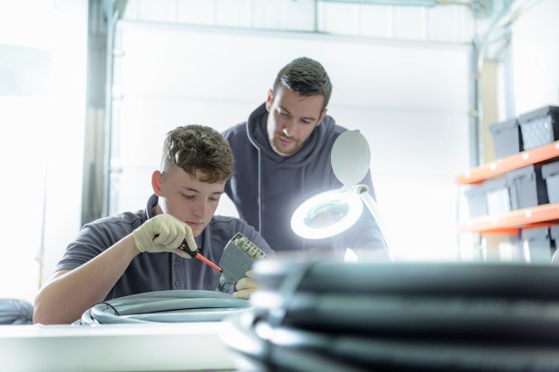 two men are working on a piece of equipment with a magnifying glass