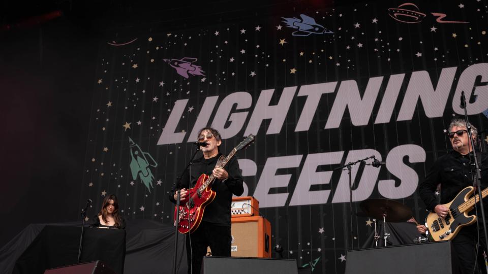 a man playing a guitar in front of a sign that says lightning reeds