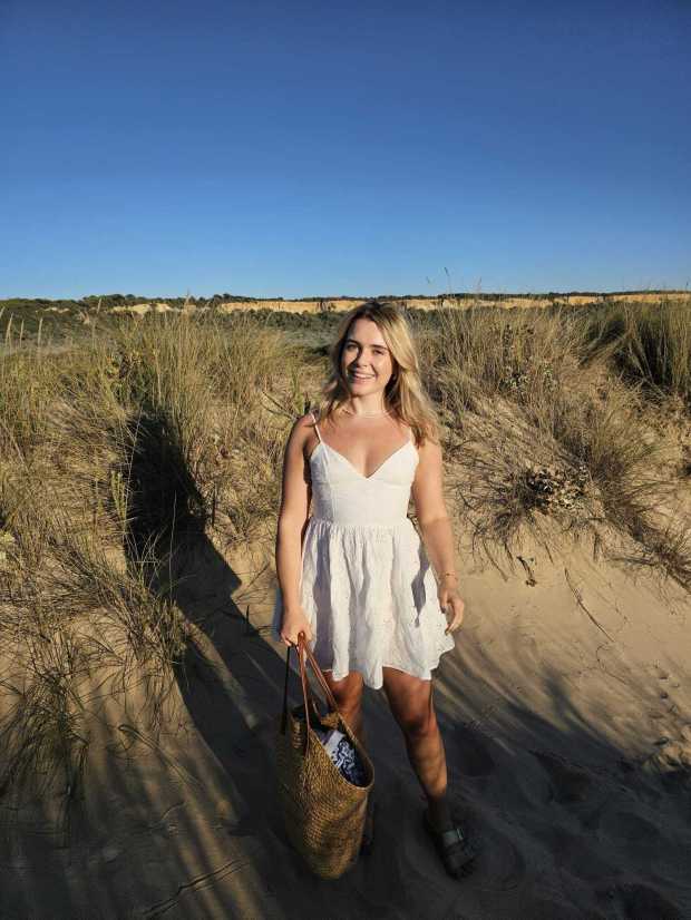 a woman in a white dress is standing on a sandy beach