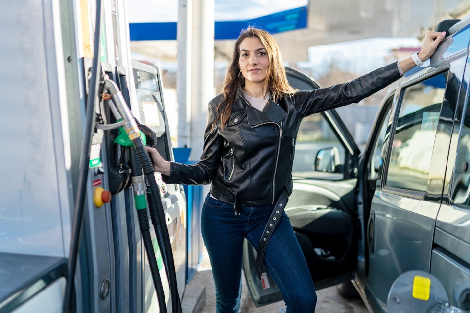 a woman is standing next to a car at a gas station