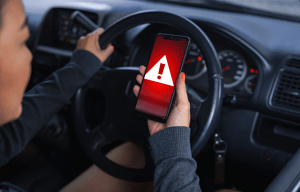 a woman in a car is holding a cell phone with an exclamation point on the screen