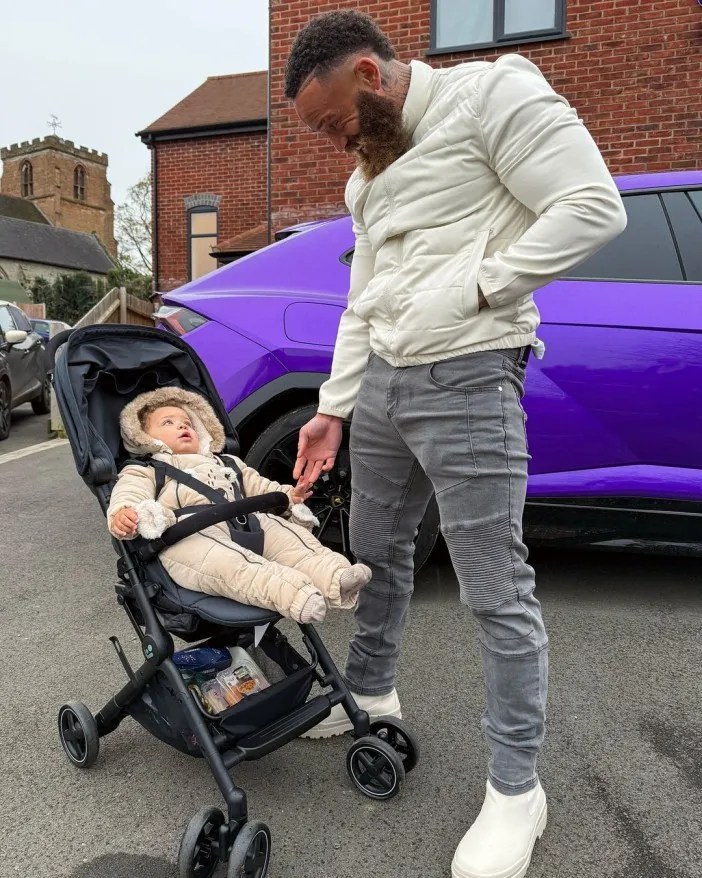 Man looking at baby in stroller next to purple car.