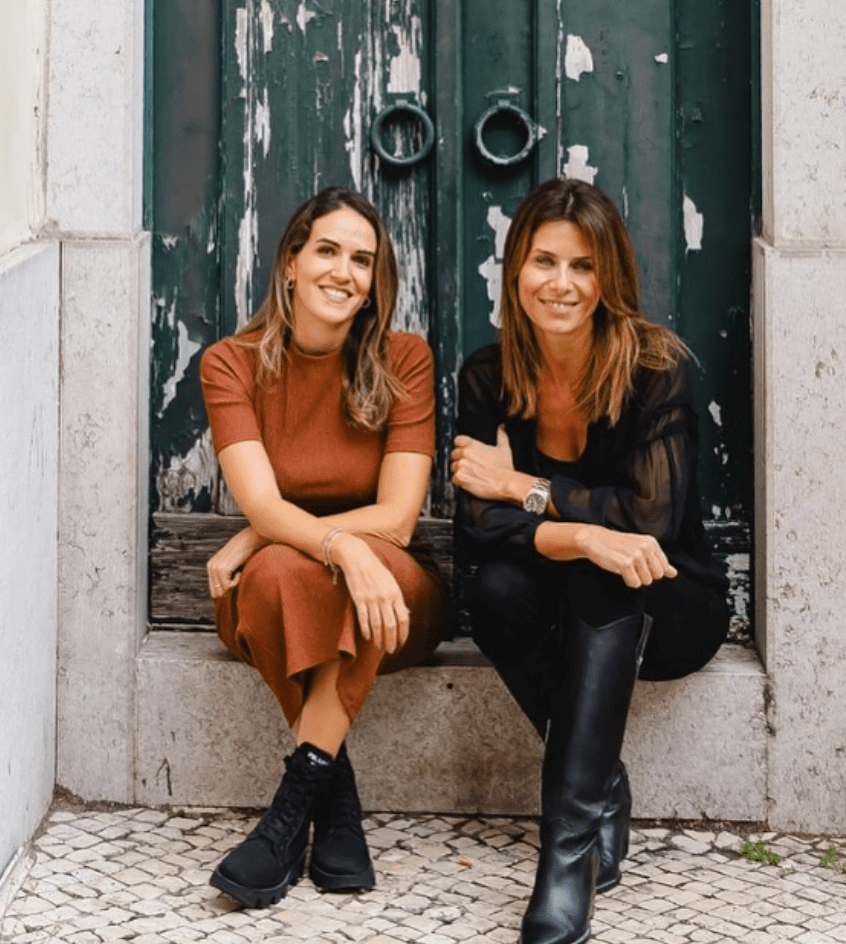 two women sit next to each other in front of a green door