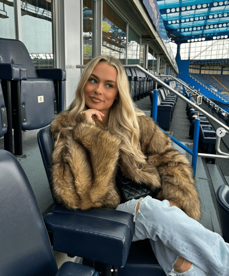 a woman wearing a fur coat sits in a stadium seat number 8