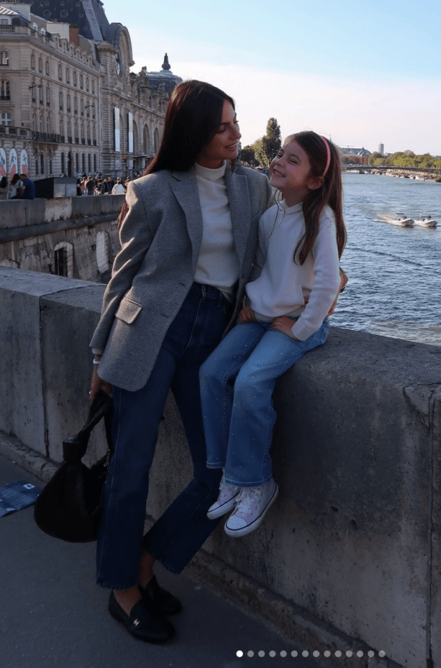 a woman and a little girl are sitting on a wall overlooking a river