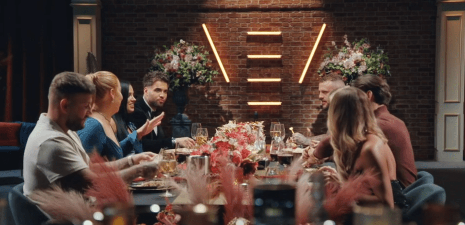 a group of people sitting at a table with a neon sign in the background