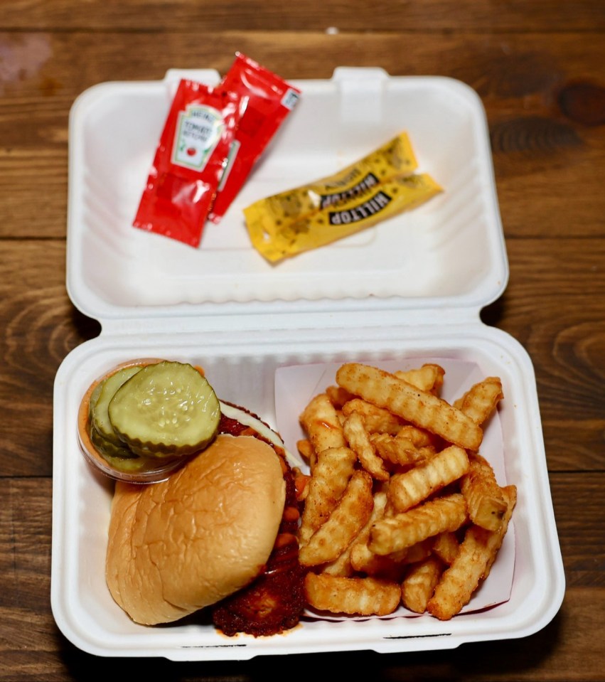 a hamburger and french fries in a styrofoam container with ketchup and mustard