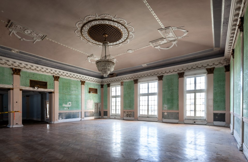 an empty room with green walls and a chandelier hanging from the ceiling