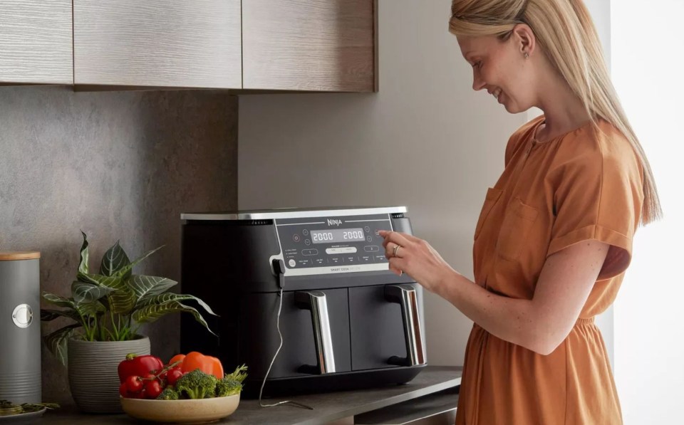 a woman is using a ninja air fryer in a kitchen