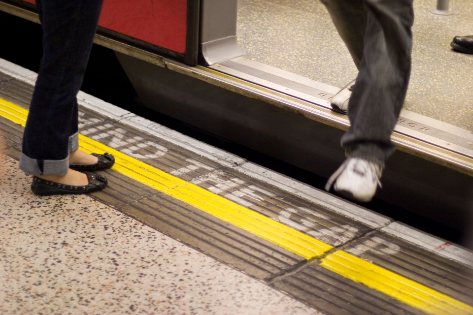 a person standing next to a sign that says " mind the gap "