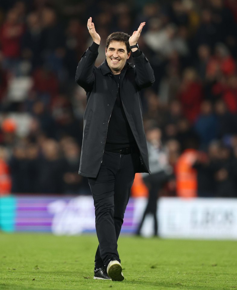 a man in a black coat applauds on a soccer field