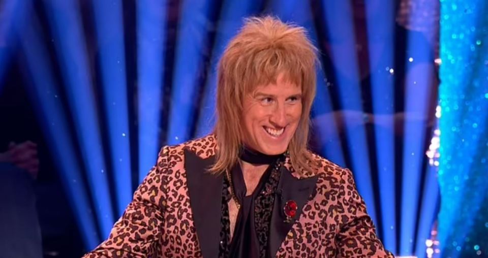 a man in a leopard print suit is smiling on a stage .