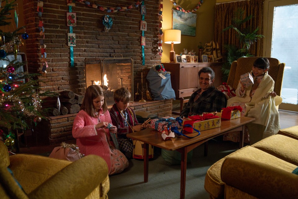 a family sits in front of a fireplace decorated for christmas