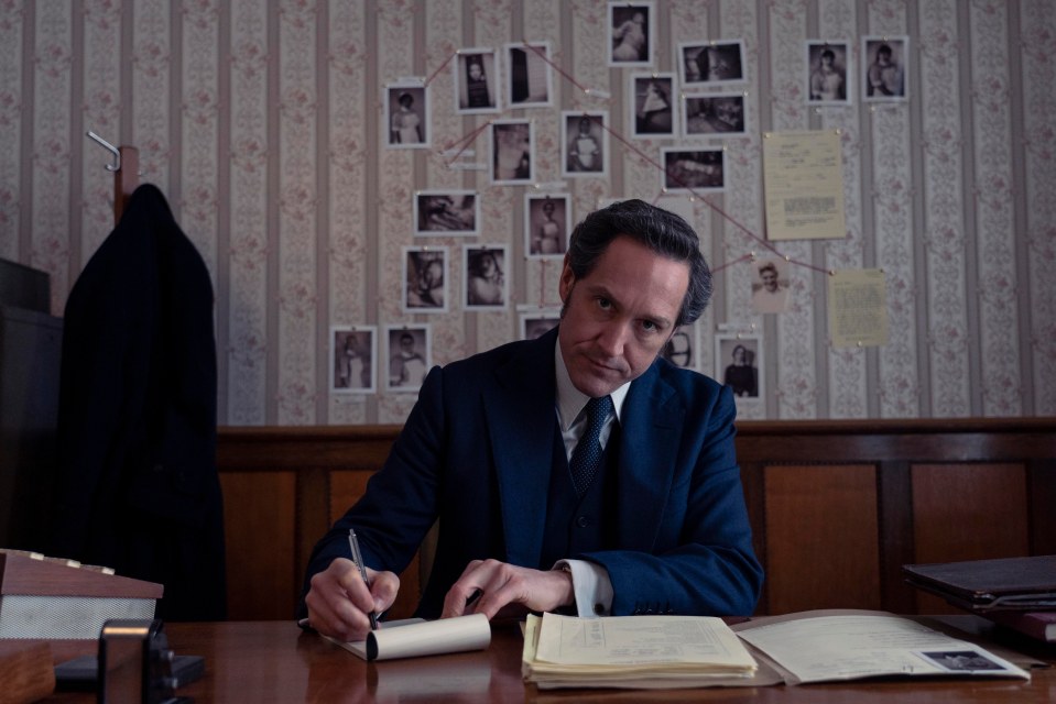 a man in a suit sits at a desk writing on a piece of paper