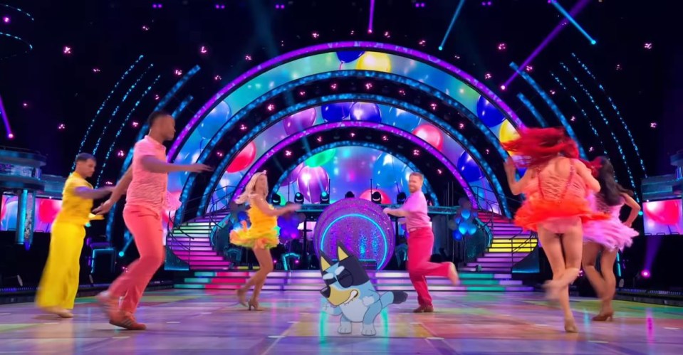 a group of people are dancing on a stage with a blue dog in the foreground