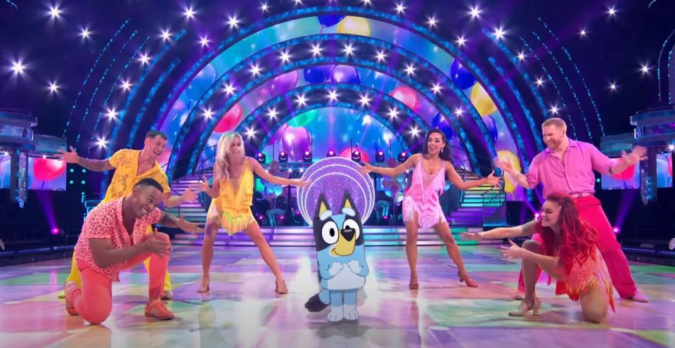 a group of people are dancing on a stage with a blue dog in the middle