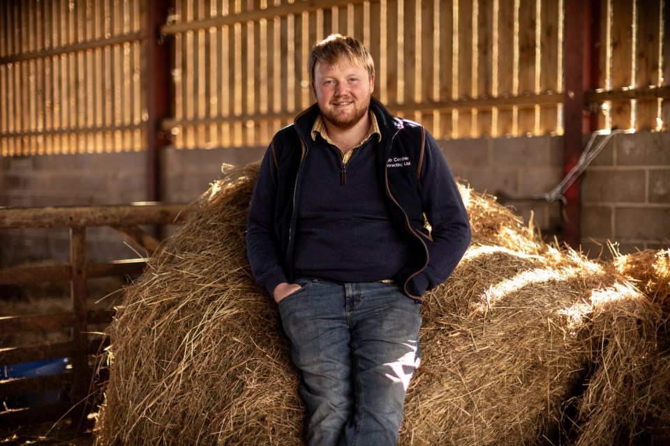 a man sitting on a bale of hay wearing a jacket that says ' j. scott ' on it