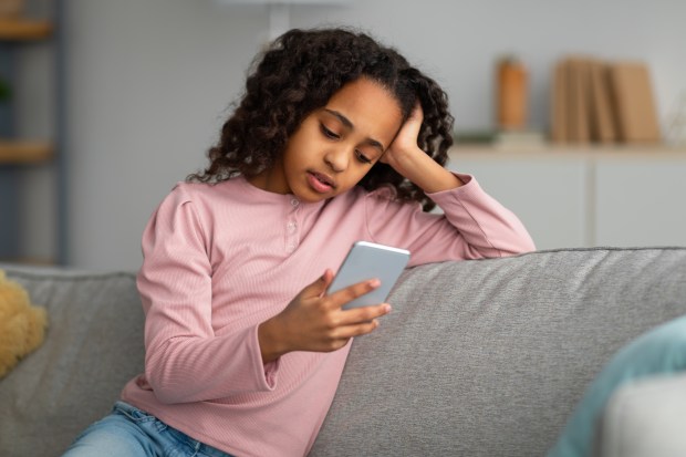 a young girl is sitting on a couch looking at her phone