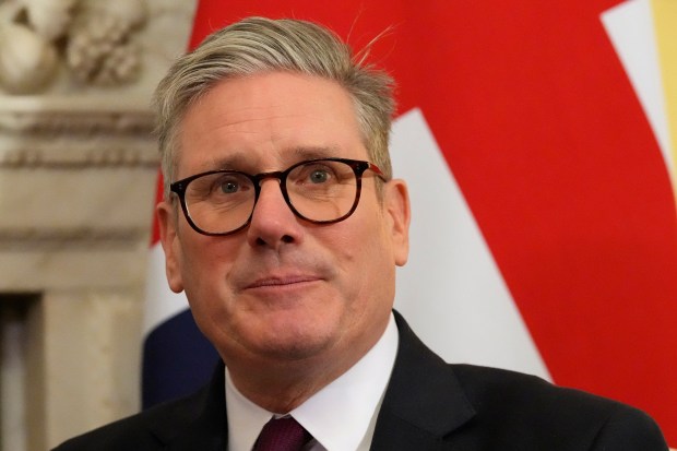 a man wearing glasses and a suit stands in front of a red white and blue flag