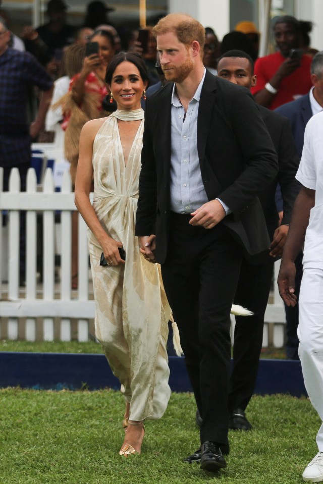 a man in a suit and a woman in a white dress are walking on the grass