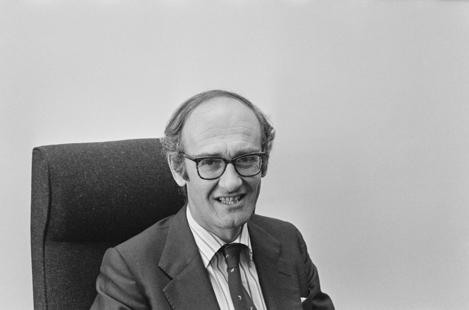 a man wearing glasses and a suit sits in a chair