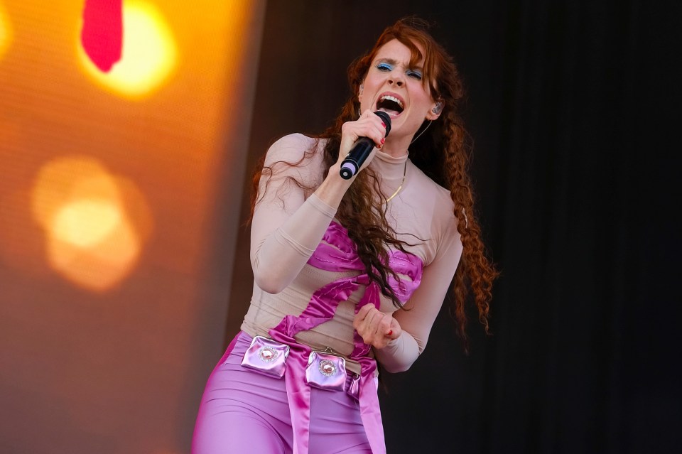 a woman singing into a microphone in a pink outfit