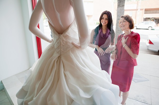 two women are looking at a wedding dress on a mannequin