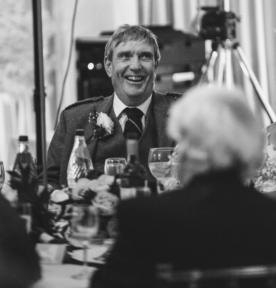 a man in a kilt laughs while sitting at a table