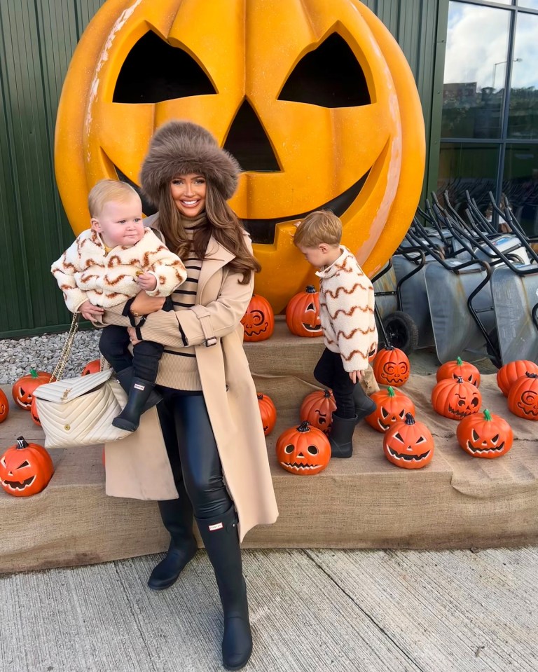 a woman holds two children in front of a large pumpkin