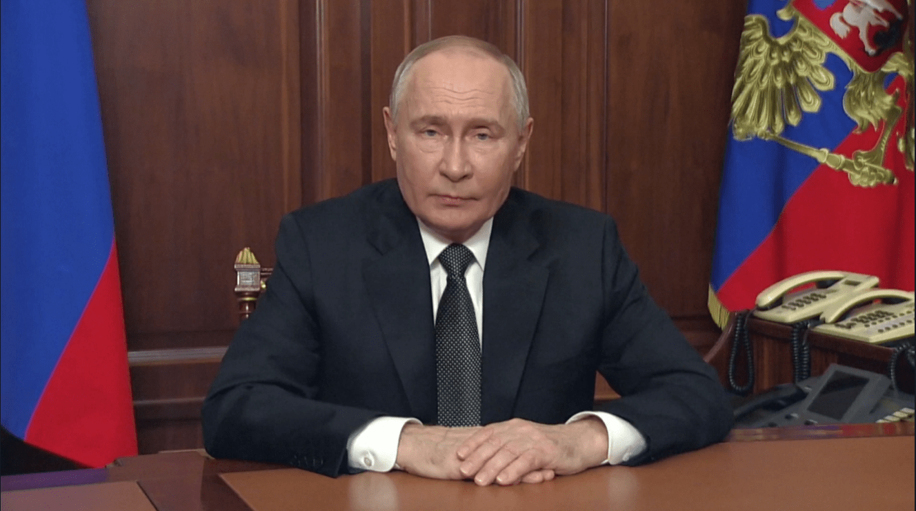 a man in a suit and tie sits at a desk with his hands folded