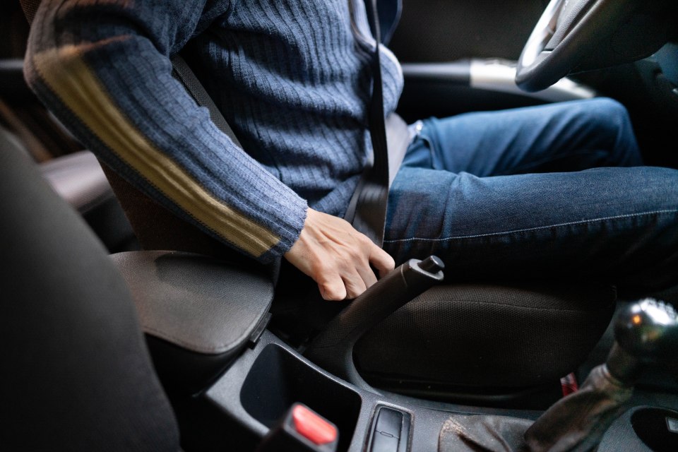 a man in a blue sweater is putting on his seat belt