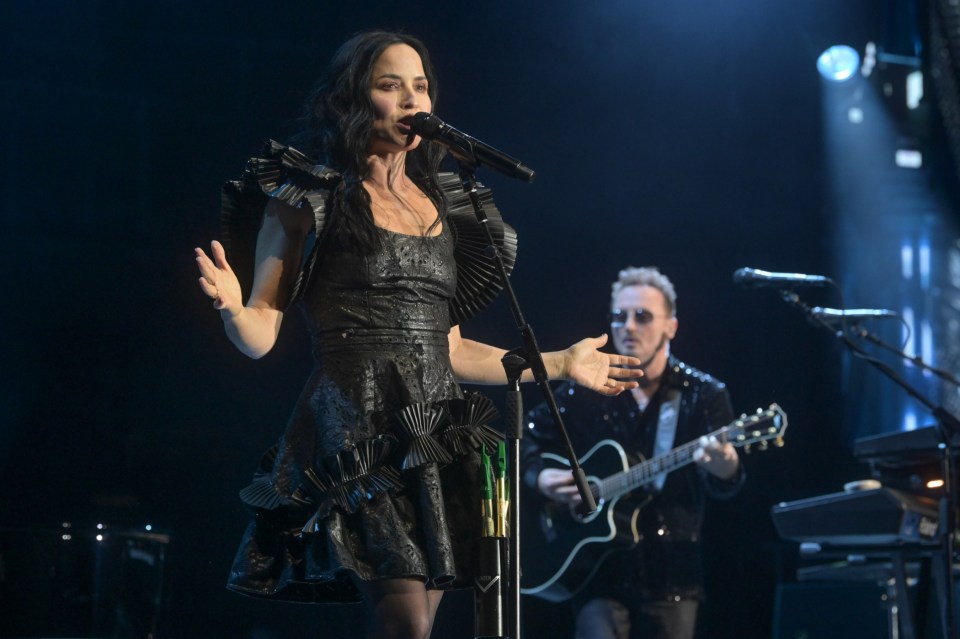 a woman singing into a microphone with a man playing a guitar behind her