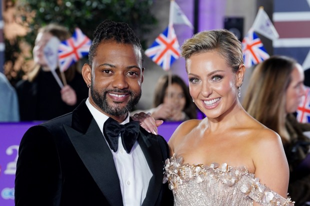 a man in a tuxedo and a woman in a dress pose on a red carpet