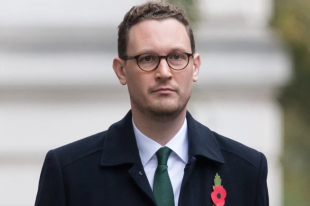 a man in a black coat and green tie has a poppy pinned to his jacket