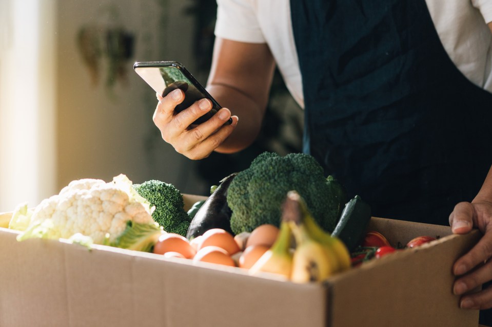 a person is holding a box of vegetables and looking at their phone