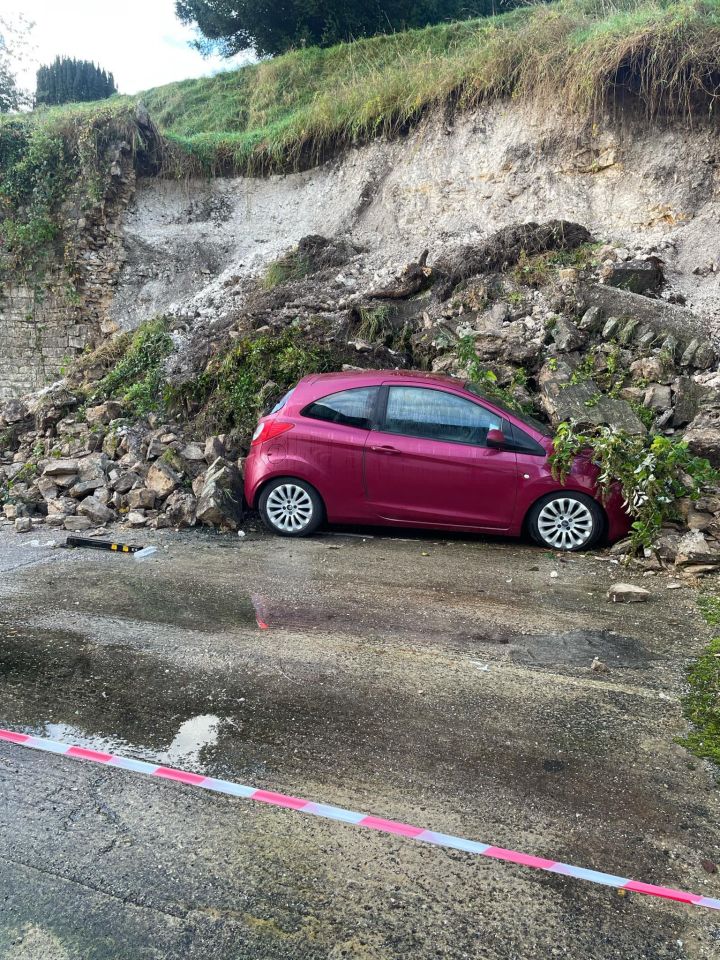 a pink car is parked in front of a rock wall