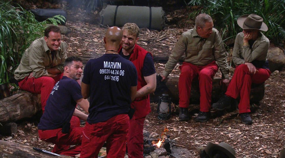 a group of men sitting around a campfire with one man wearing a shirt that says marvin